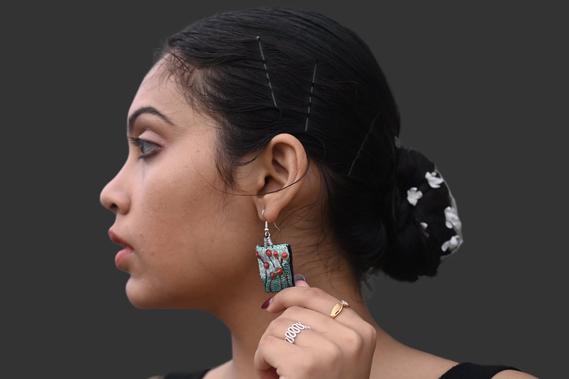 Woman wearing earrings and a ring against a textured wall background